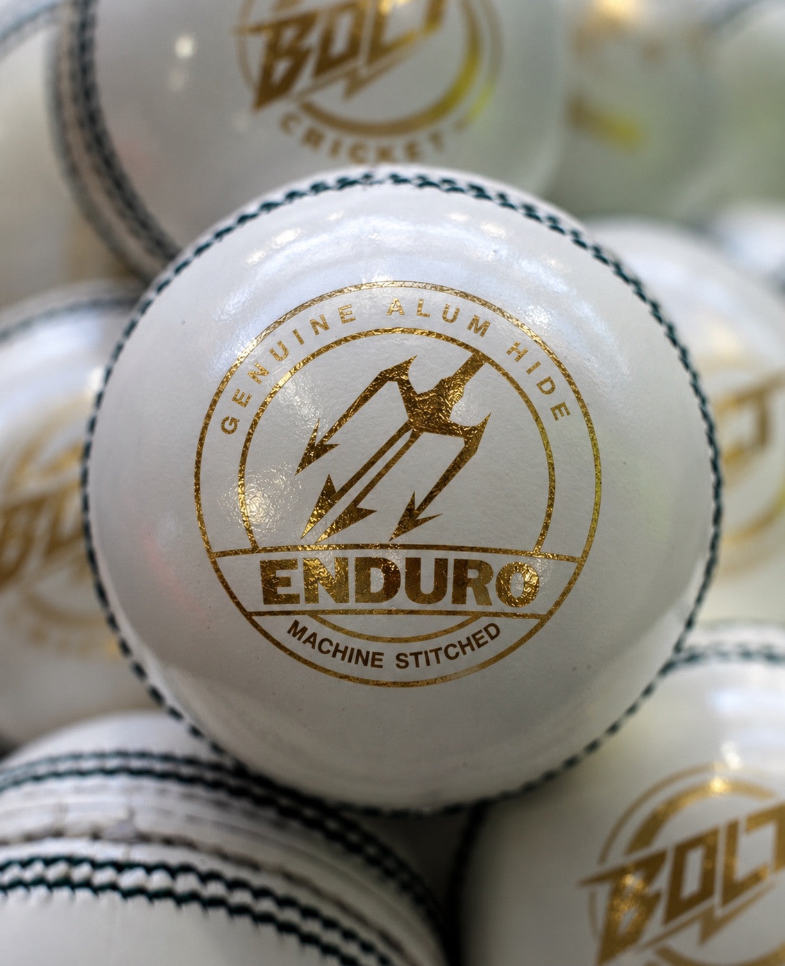 White Bolt Enduro cricket ball with gold Enduro Machine Stitched marking, among other white balls